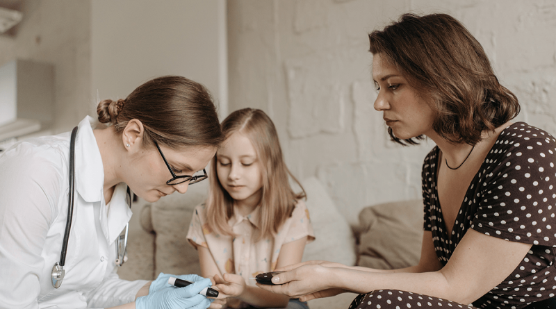 A doctor administering a diabetic blood test to a child while their parent looks on.
